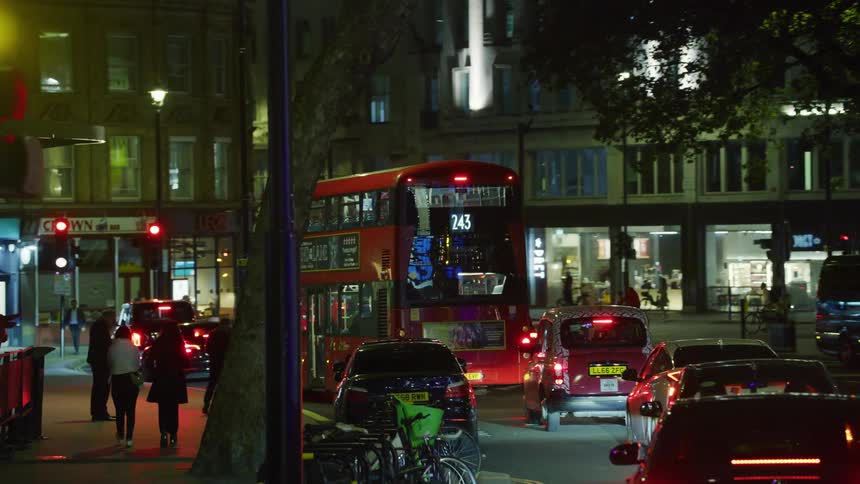 Red double decker bus drives on city street at night