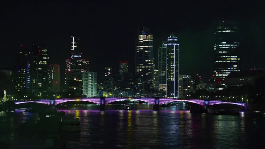 The skyline of london bridge is illuminated with purple light at night
