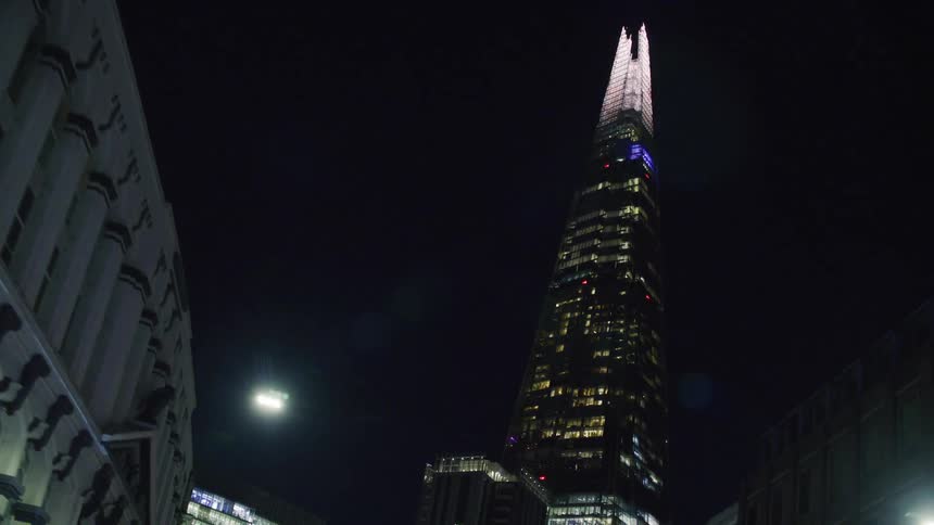 Brightly lit pointed skyscraper towers over nearby buildings at night
