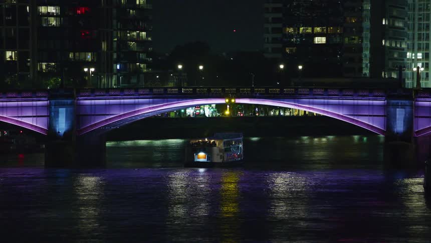 A ferry runs under the bridge at night