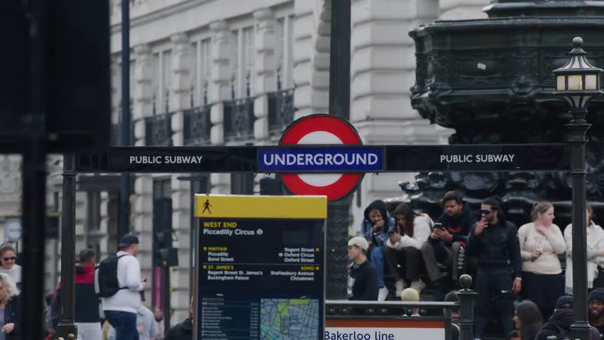 View of a train station sign in the midst of a public square with a crowd of people