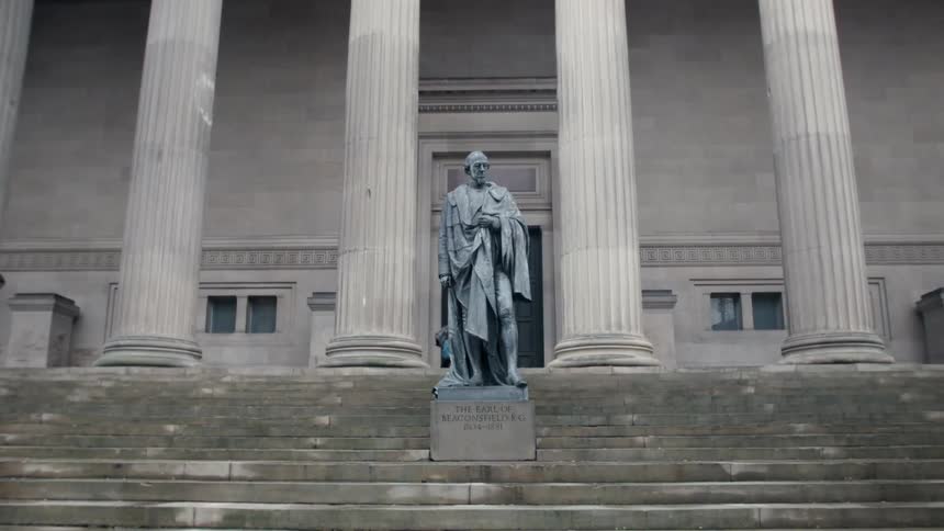 A statue of a man sits on the steps of a building with large columns