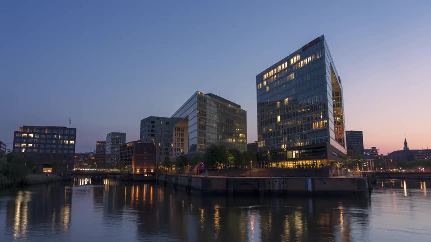 Modern buildings by the edge of a lake with the day darkening in timelapse