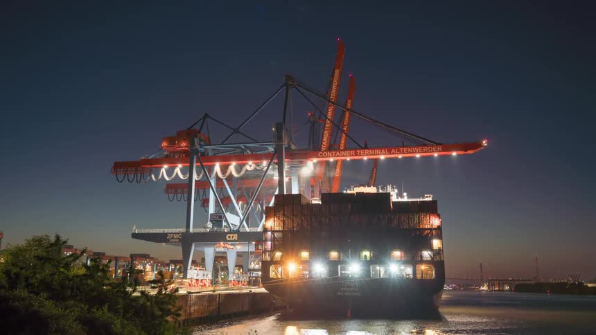 Cranes at a port lifting containers from a ship at night in timelapse