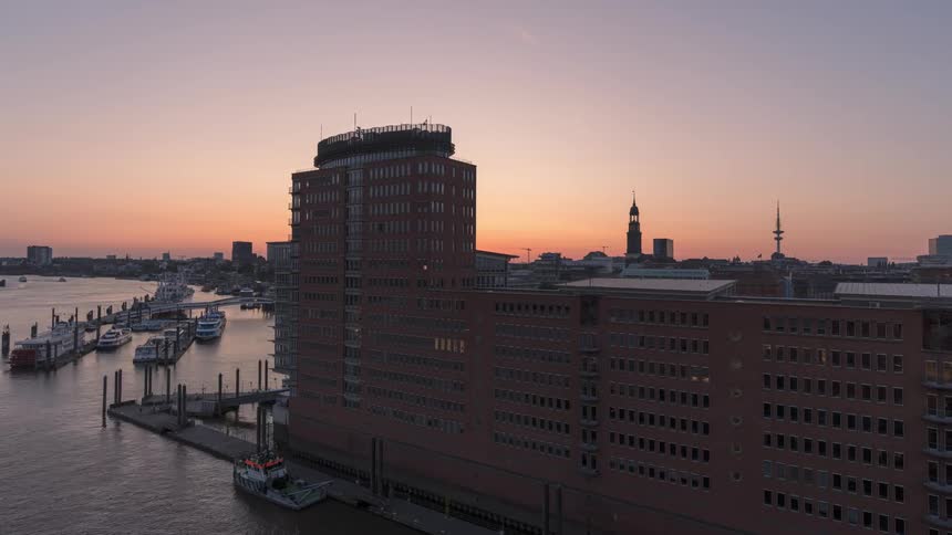 Panorama of a metropolitan city by the sea in timelapse with the sun setting on the horizon and darkness falling