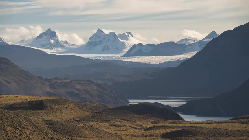 Mountain range with glaciers and snow by the edge of a lake with clouds passing in timelapse