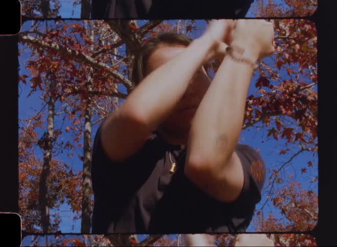 Woman moves her hands through a series of motions while standing under a tree with fall foliage