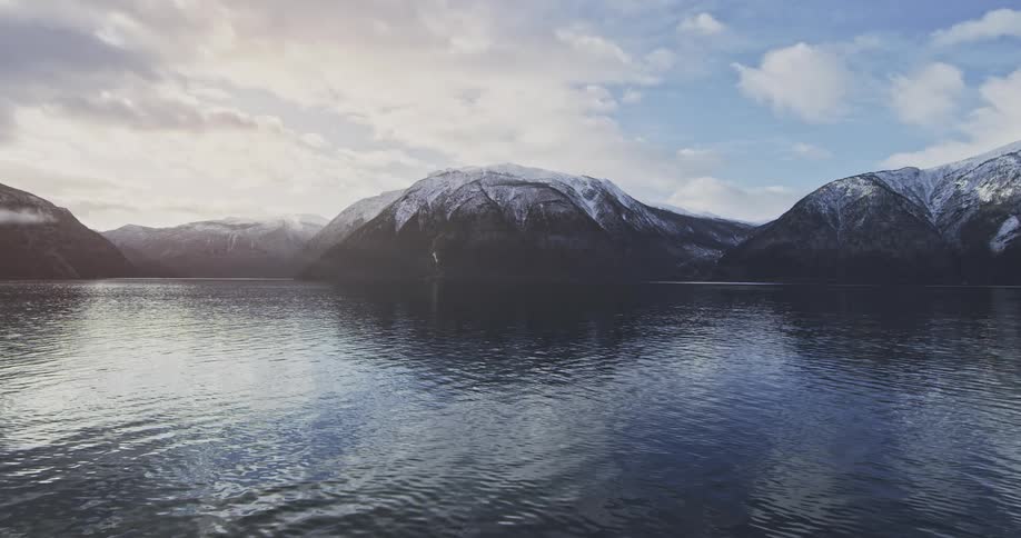 Panorama of a lake in slow motion with mountain ranges around it covered in snow during the day