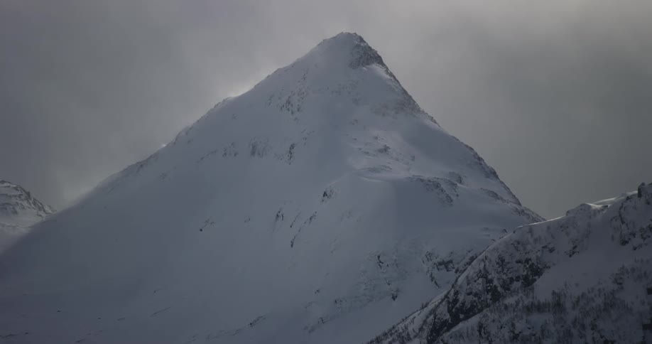 A mountai in the winter completely covered in snow with a dark cloudy sky
