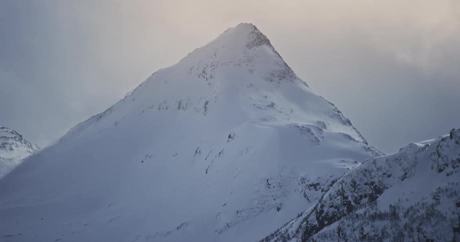 Clouds flow across peak of snow covered mountain in mountain range