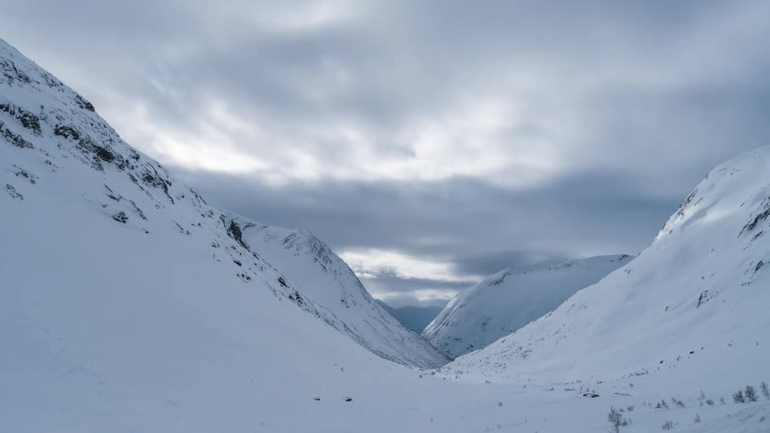 Mountains covered in snow on a cloudy day with clouds passing by in timelapse