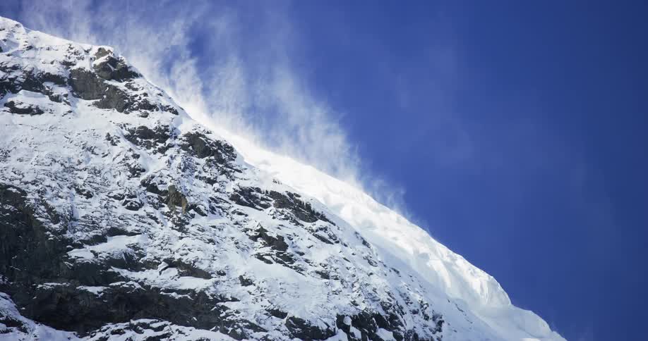 The wind blows snow on a mountain top in a clear sunny day