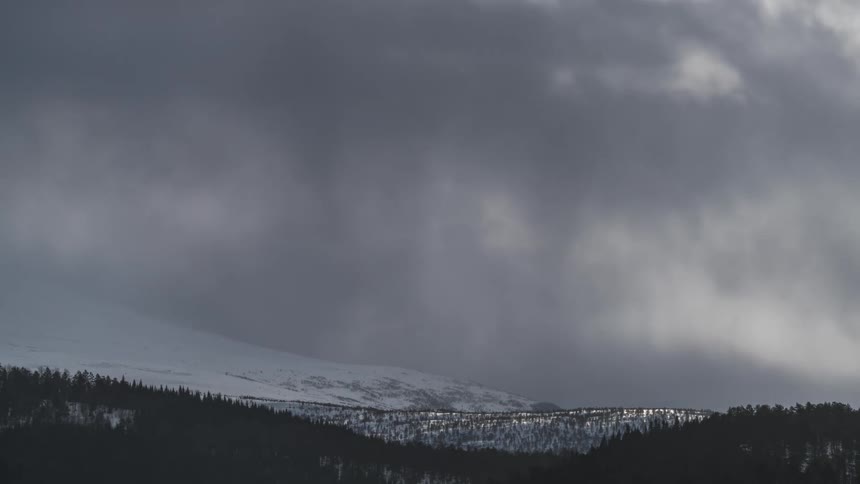 Panorama of mountain ranges with snowcovered forests and storm clouds passing by in timelapse