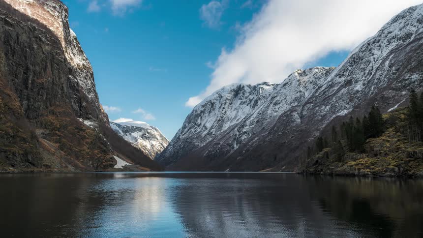 Rippling lake surrounded by mountains reflects the passing clouds