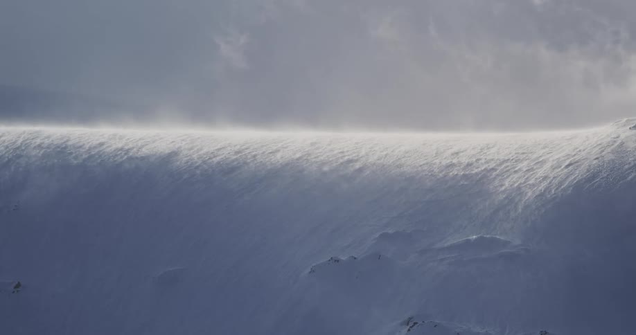 Wind blows snow across a mountain