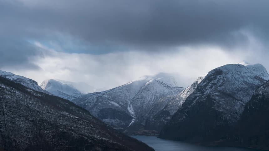 mountain ranges with snow surrounding a deep fjord on a cloudy day in timelapse