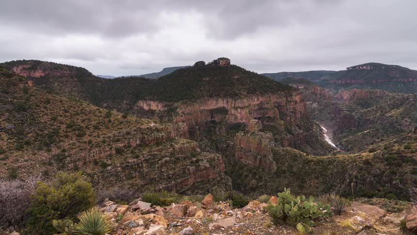 A rugged and scenic landscape of steep rocky cliffs and a river under an overcast sky