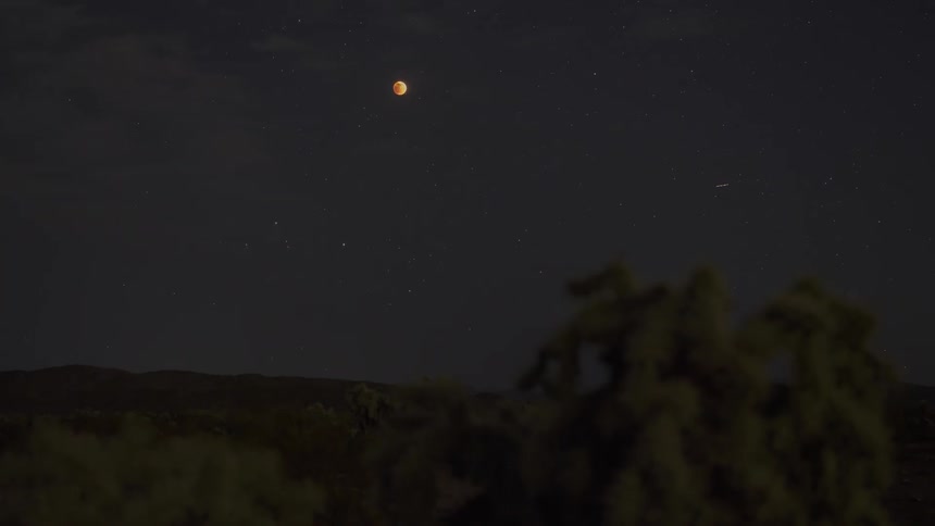 Panorama at night of mountain ranges in the background and the moon rising into the sky in timelapse