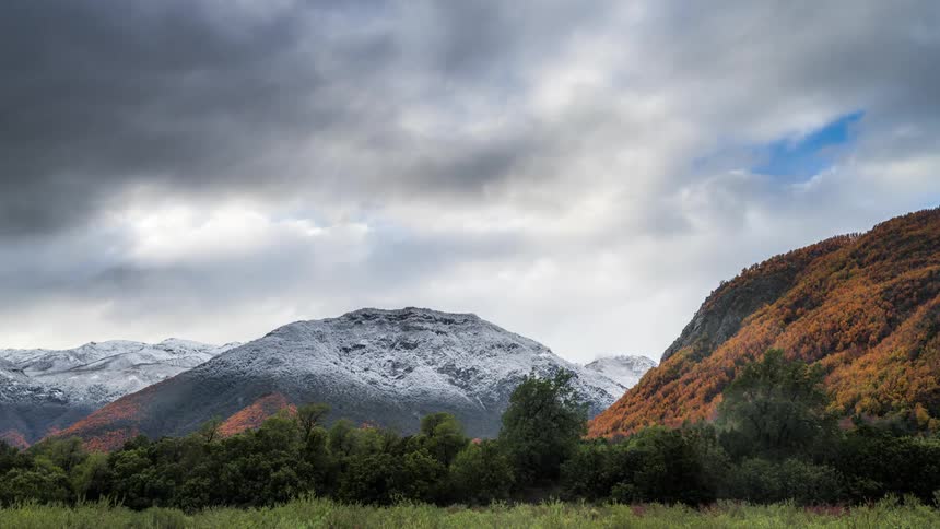 Time lapse of cloud movement over mountains covered in snow and fall colors