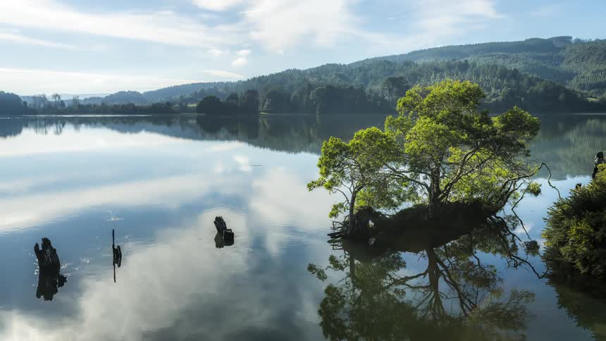Landscape of a reflective lake with clouds in the sky and mountain ranges around it