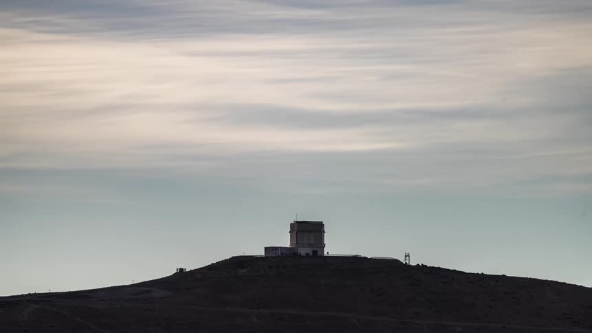 A telescope on a hill with clouds moving by