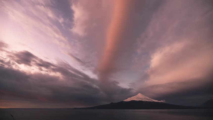 clouds during sunset moving over snow covered peak on horizon