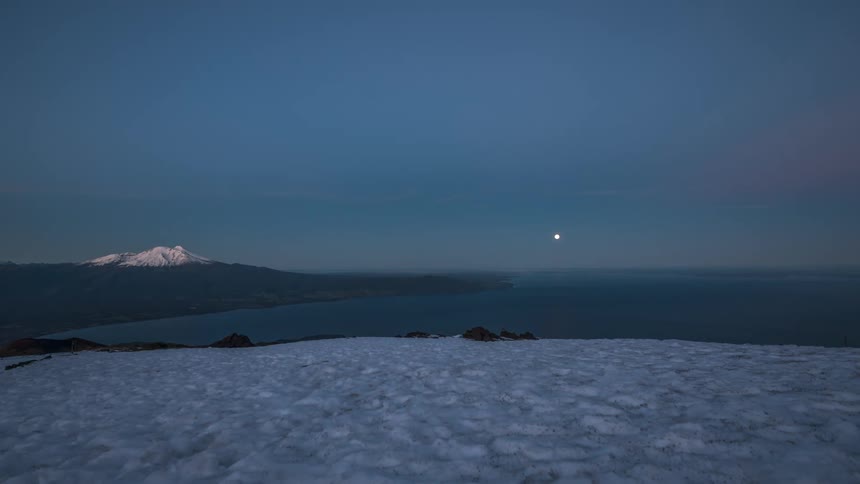 timelapse view of a snowcovered mountain as the moon sets and the day brightens during dawn