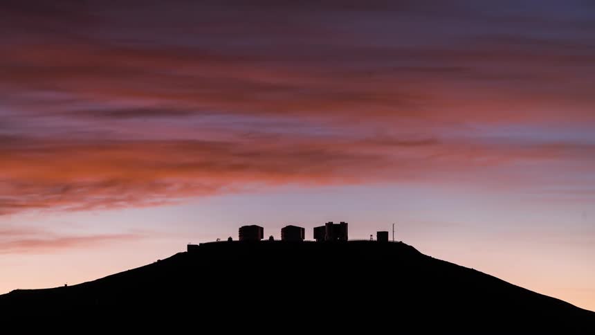 colorful clouds during sunset over an astronomical observatory with the crescent moon setting behind it