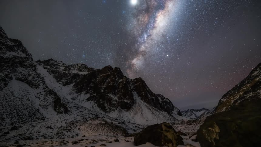 Nightsky with milkyway over snowy mountains with clouds moving in