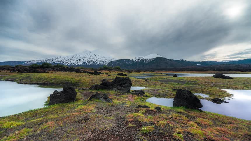 Landscape with small lakes and mountain range with snow and passing clouds