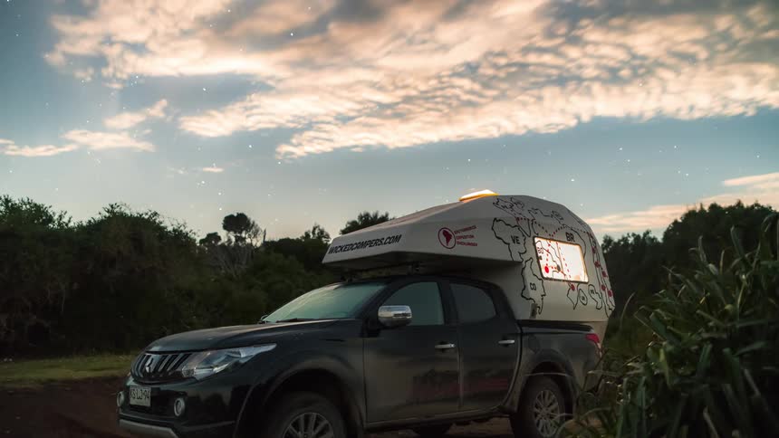 A truck with a camper sits near a forest