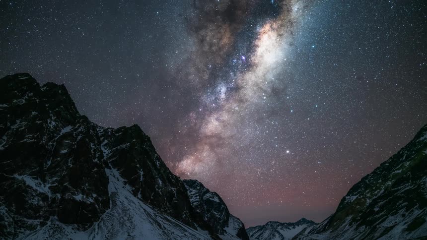 The milky way galaxy moves through the night sky over a snowy mountain range