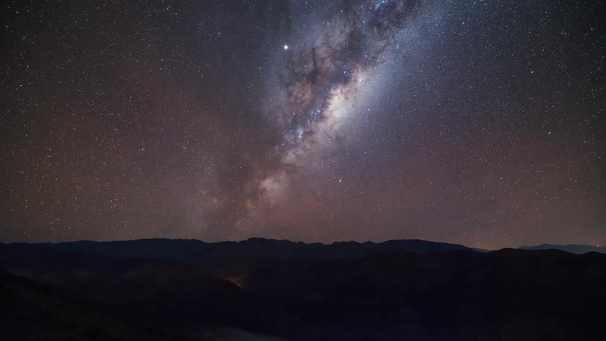 a smooth day to night transition over arid mountainous terrain revealing the milkyway