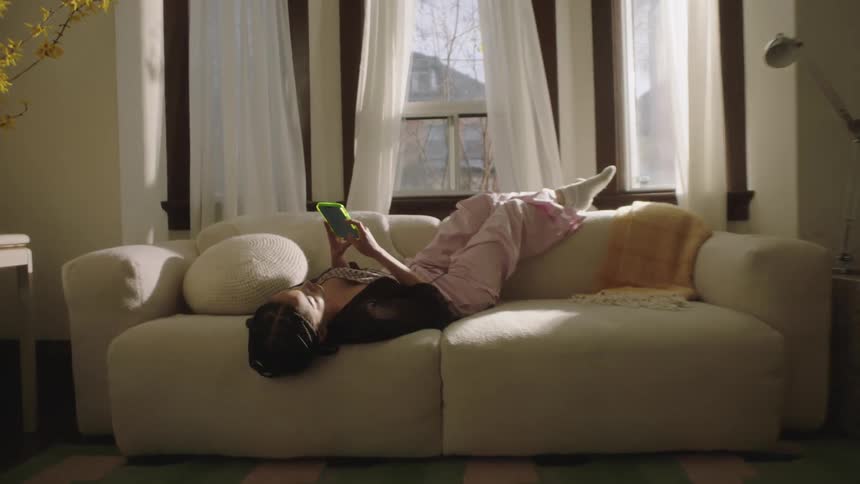 A young woman lies on the couch scrolling through her phone