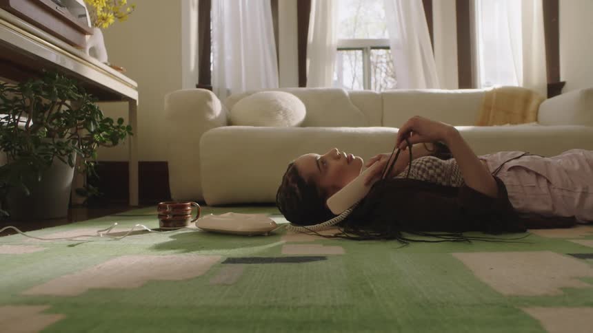 Young Woman lays on the floor playing with her hair and talking on the phone
