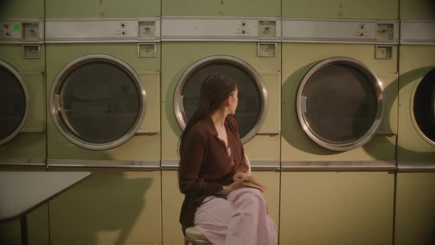 A woman reads a book as she does laundry