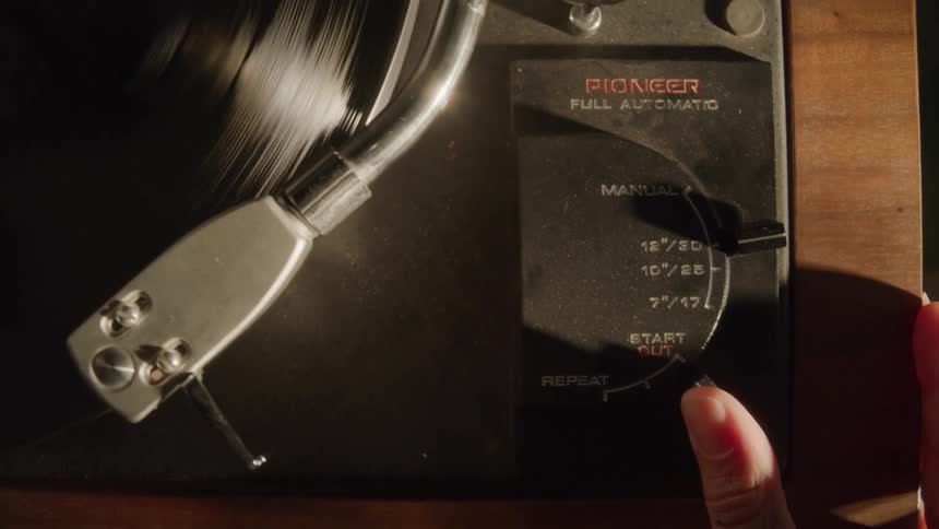 Close-Up of a woman's hand turning on a record player and dropping the needle