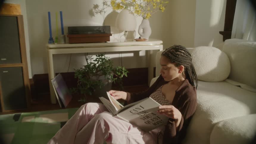 Steadicam dolly shot of  young woman sitting on the living room floor reading a book
