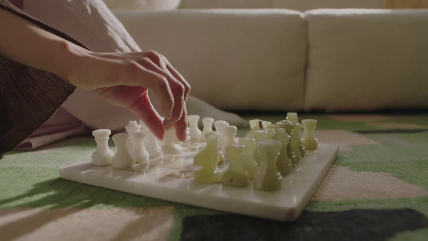 Closeup of a stone chess set on the floor with a person moving one of the pieces