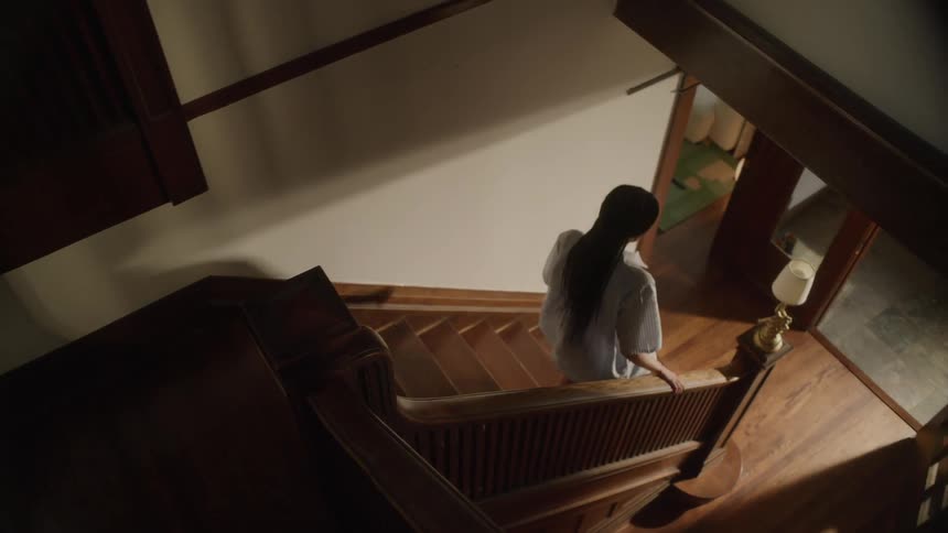 A young woman in pajamas walking down the stairs of her home in the morning light