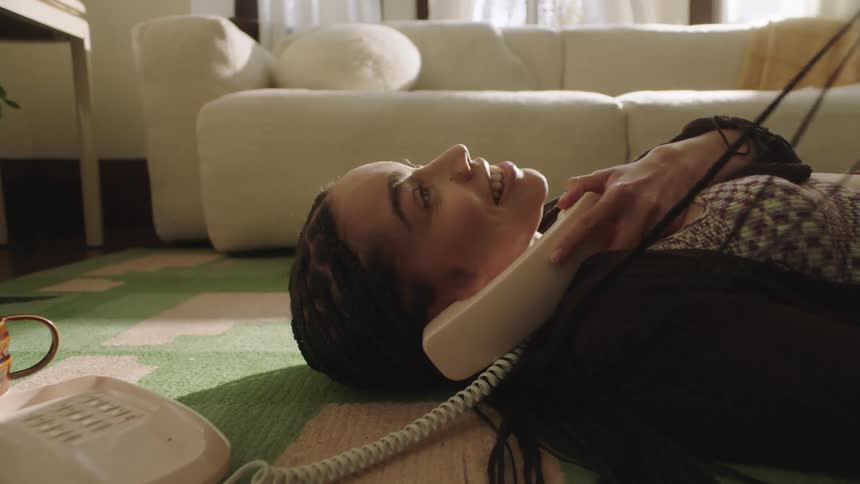 Young Woman laying on the floor playing with her hair and talking on a vintage phone