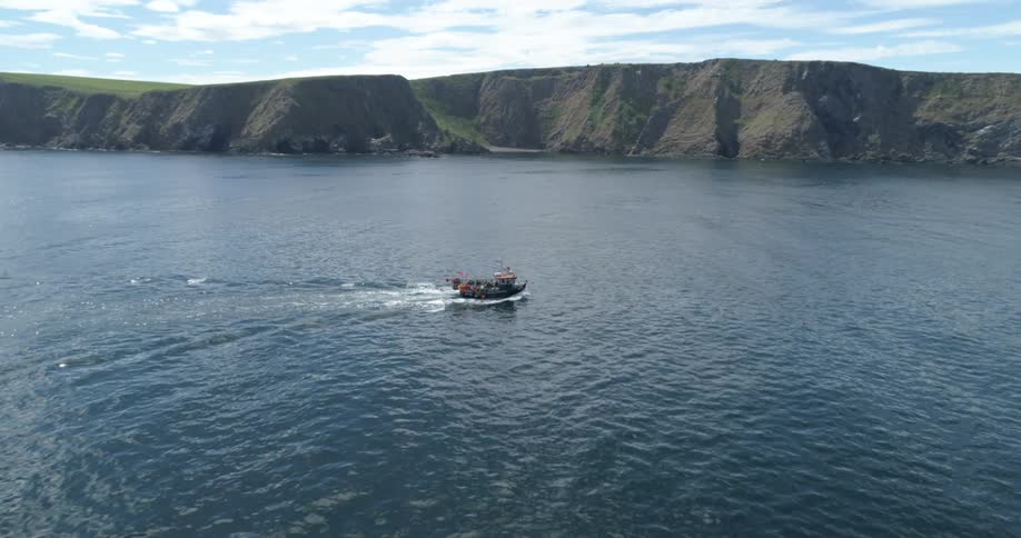 Aerial of boat traveling across water with the coastline in the background