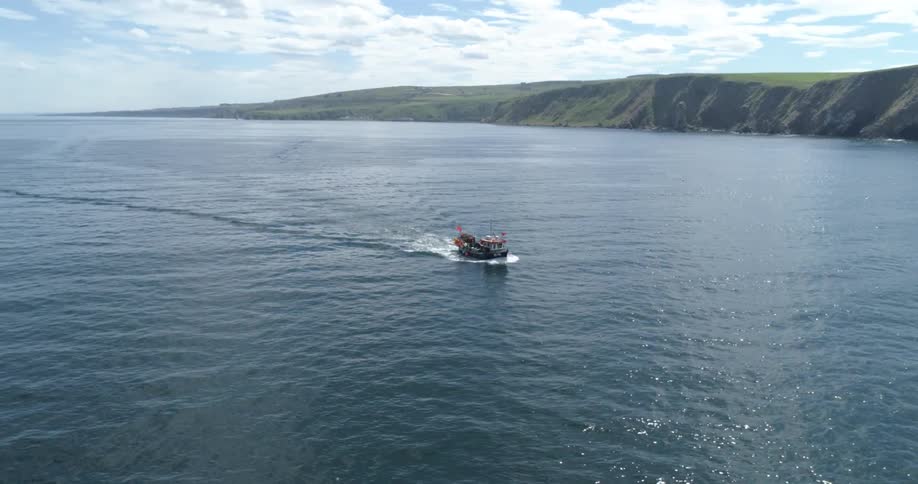 A fishing boat sailing near the mountainous coast during the day