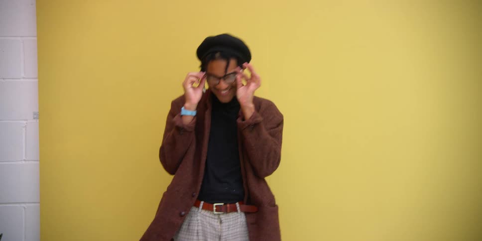 A black man laughs and spins around in front of a yellow background