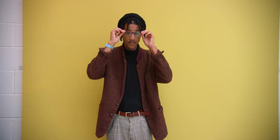 Model man adjusting his clothes and glasses and posing on a yellow background