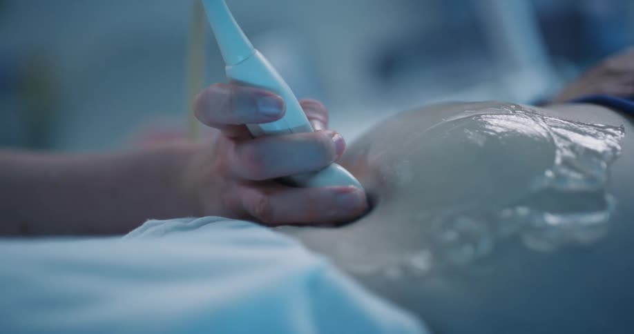 Hand holding a device with gel over the belly of a pregnant woman performing an ultrasound