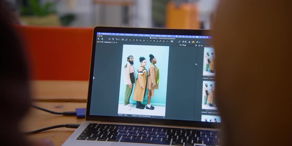 A person viewing a fashion photo on a laptop with three models in stylish outfits