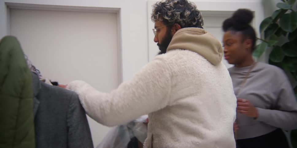 A man and a woman hang coats on a clothing hanger rack