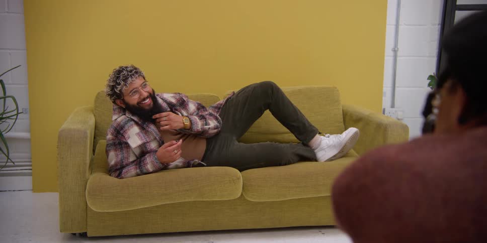 A person lying on a yellow couch modeling for a photographer