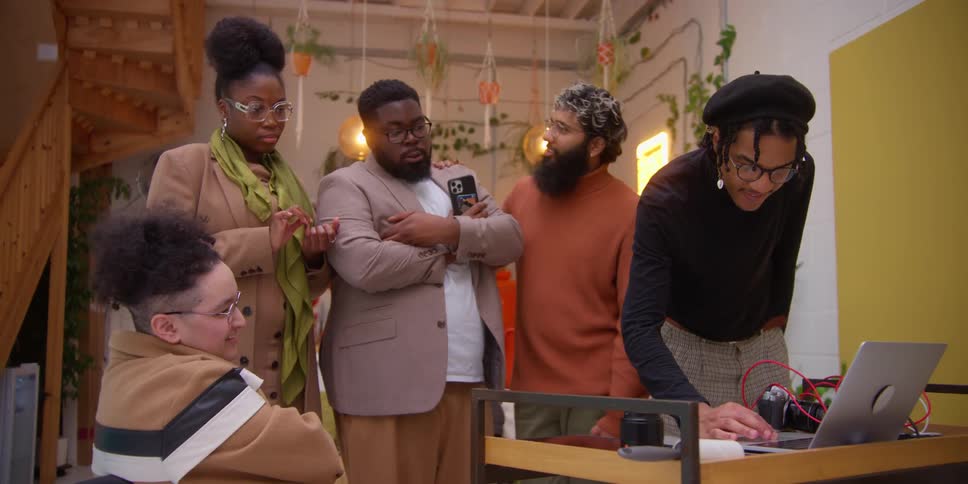 Friends including a person in a wheelchair watching one of them working on a laptop while having a conversation